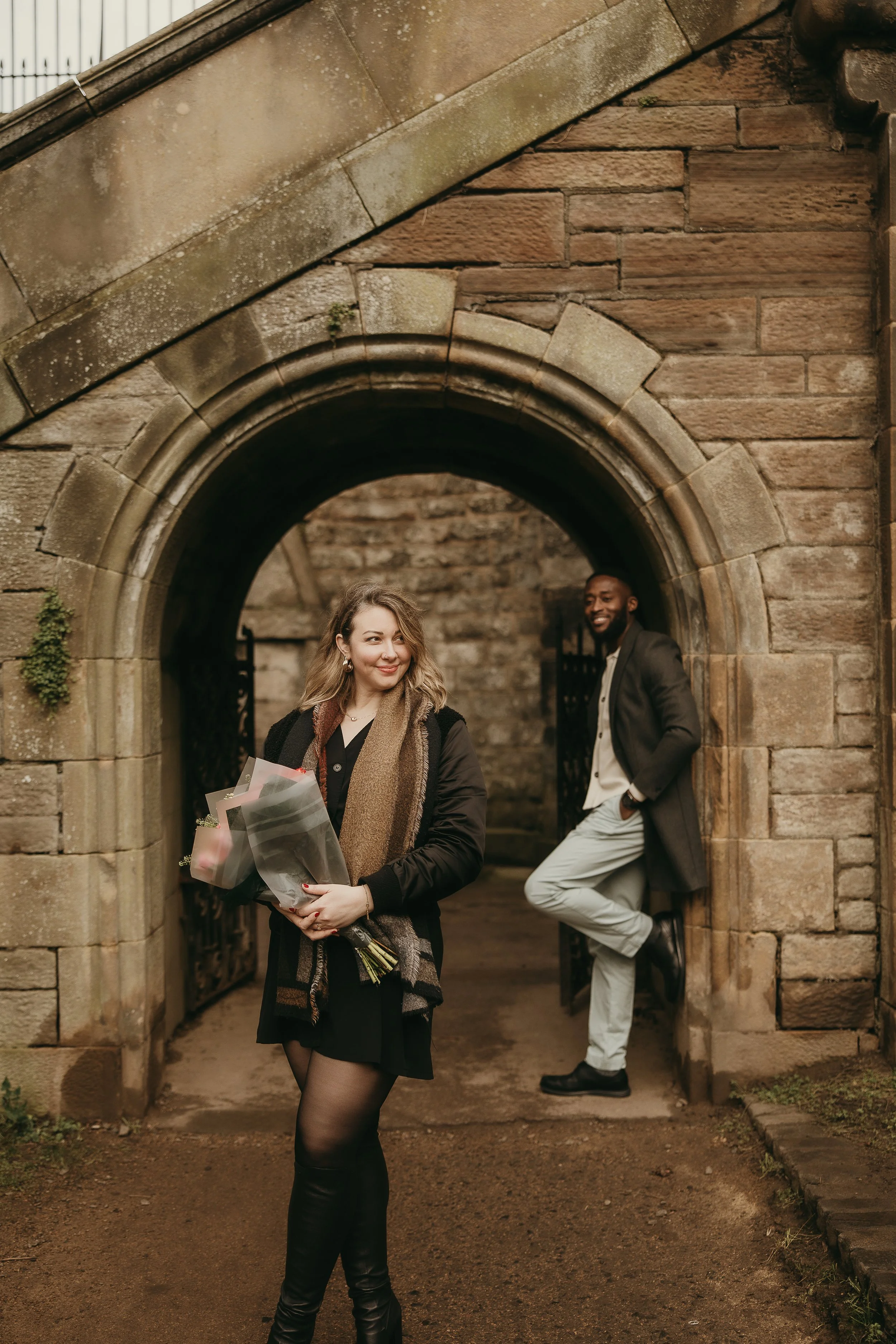 Happy couple posing with flowers and celebrating after proposal in Edinburgh , candid romantic engagement photos.