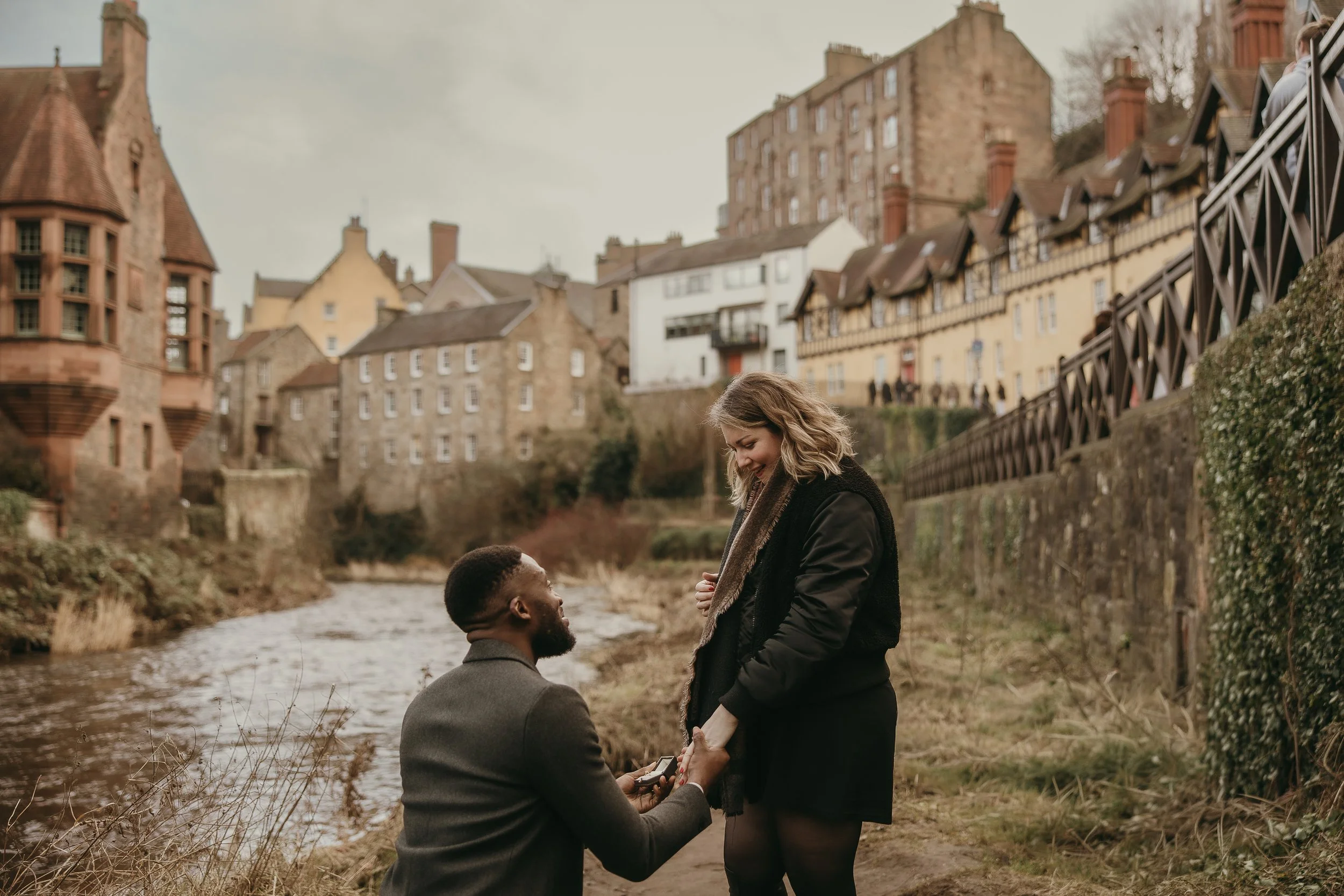 Happy just engaged couple hugging after a surprise proposal in Edinburgh with romantic natural candid photography and soft golden light.