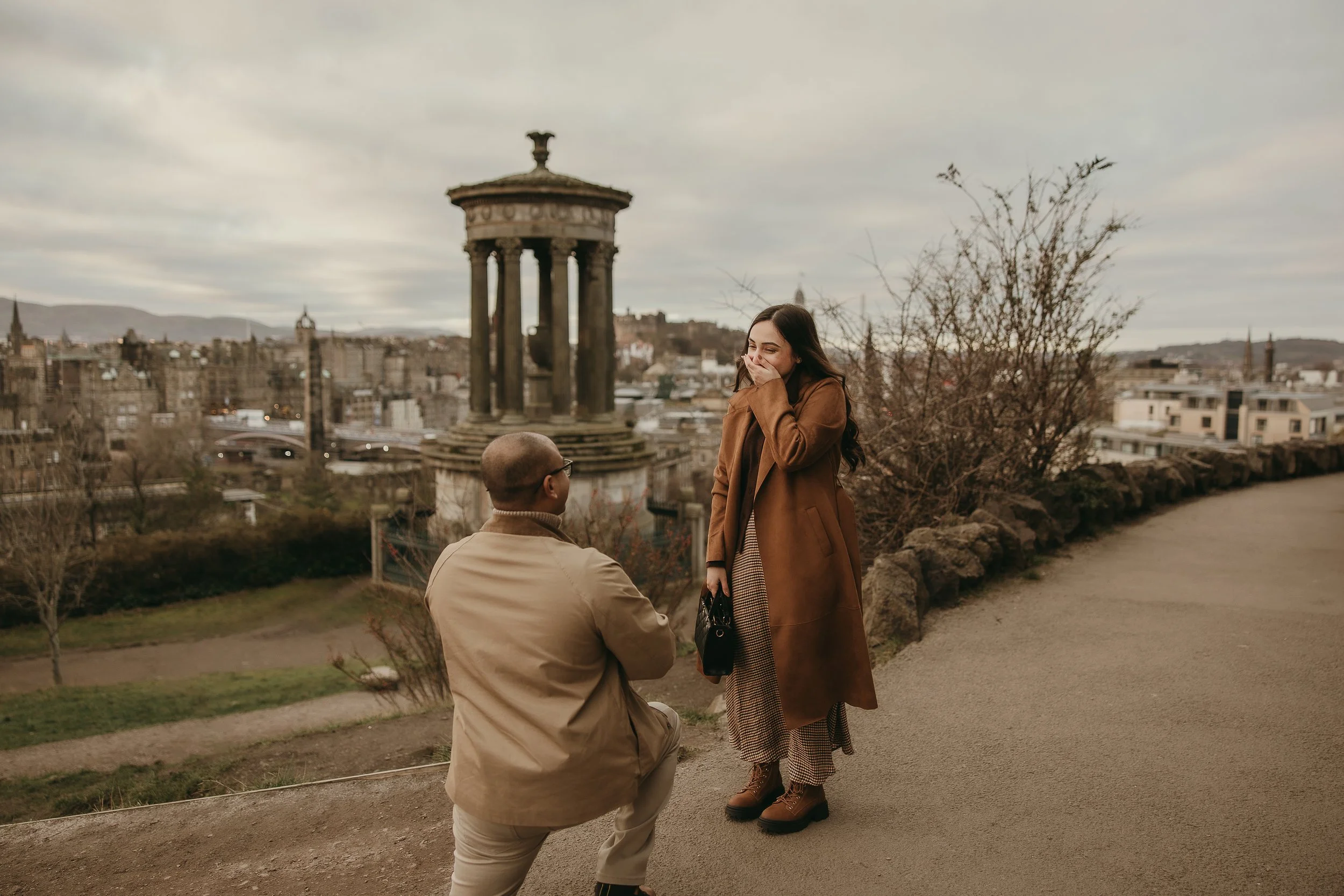 Couple holding hands and smiling in a garden with flowers and greenery.