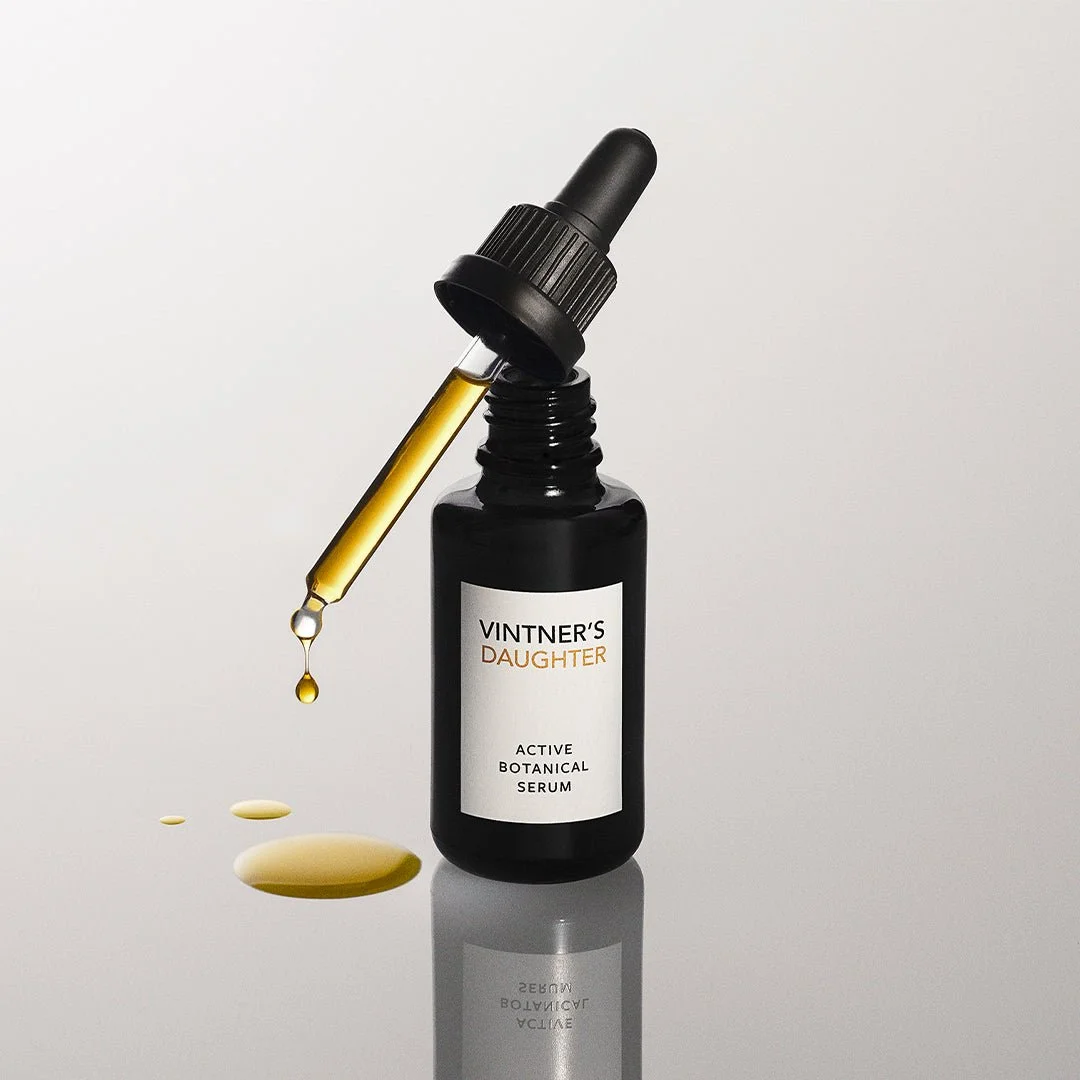 The Vintner's Daughter Active Botanical Serum bottle with its dropper, golden oil dripping onto a pale surface.