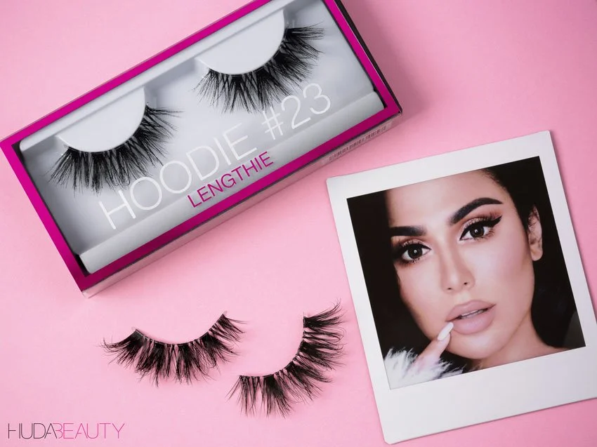 Huda Beauty Hoodie #23 false lashes beside their pink box and a polaroid of Huda Kattan.