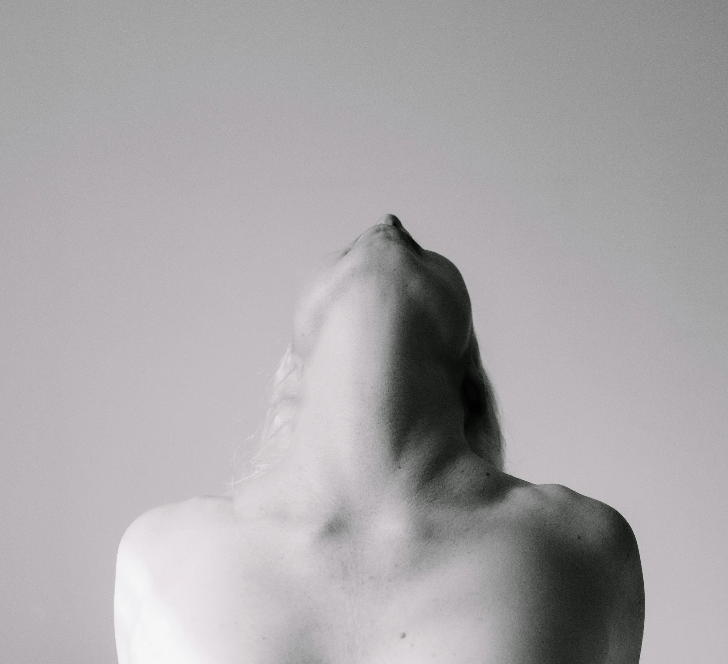 A woman photographed from behind with her head tilted back, the muscles and skin of the neck in relief, in black and white.