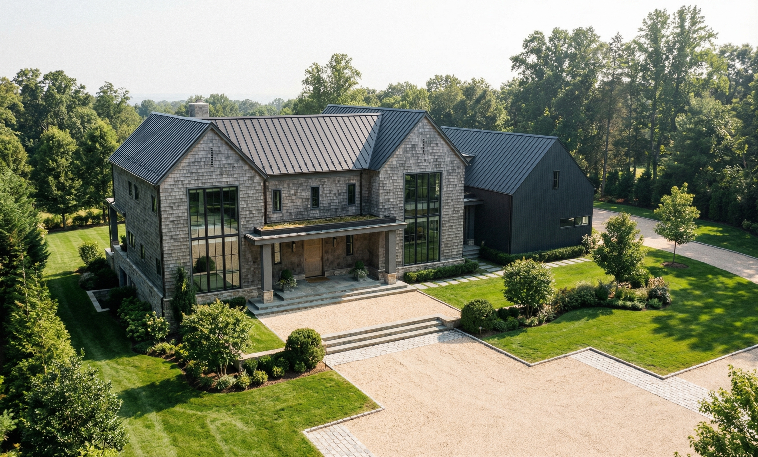 A modern two-story house with a metal roof, large glass windows, and a landscaped front yard with trees, grass, and a gravel pathway.