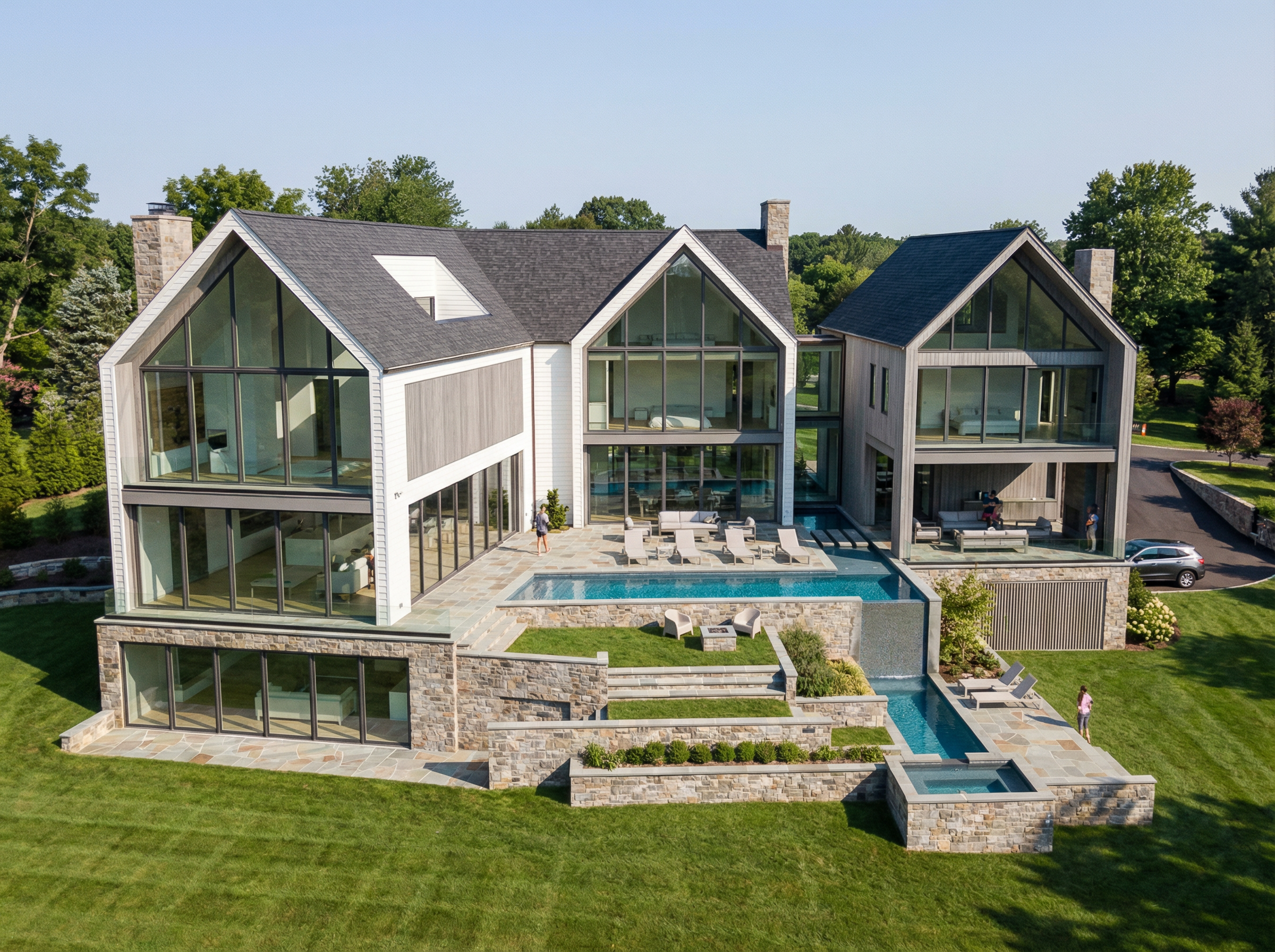 A modern house with large glass windows, stone accents, a swimming pool, and lush green lawn, on a clear day.