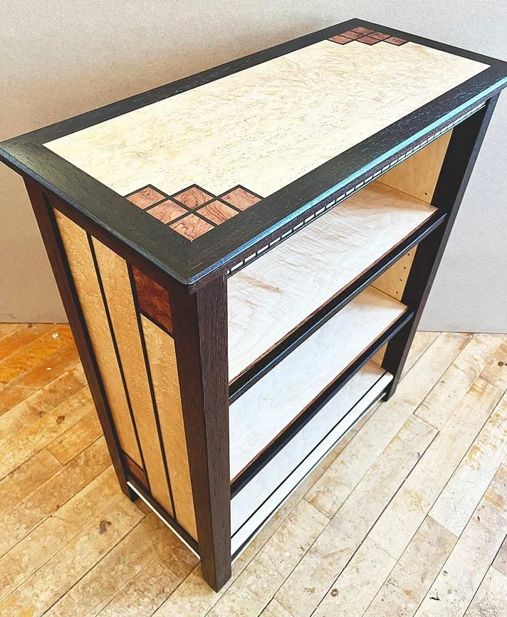 Wooden bookshelf with decorative inlay top, two shelves, and vertical paneling on sides.