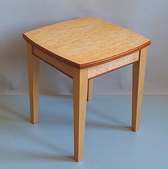 Wooden side table with a square top and four legs, light-colored wood with a darker trim on the edge of the tabletop.