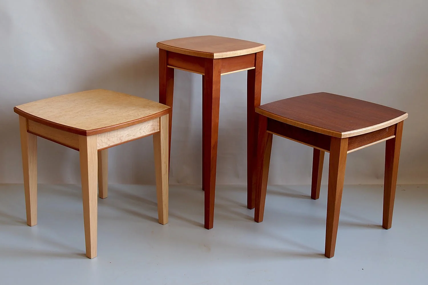 Three wooden tables with different wood finishes, arranged against a plain background.