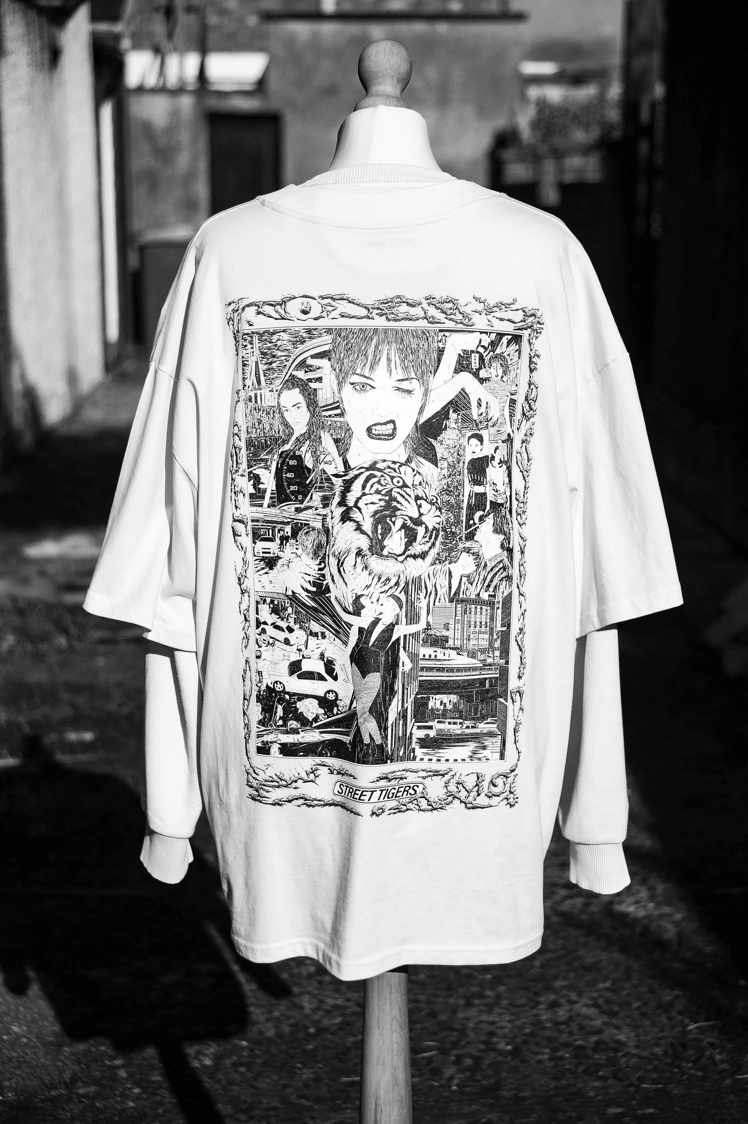 White sweatshirt on a mannequin featuring a detailed black-and-white streetwear graphic of a tiger, city scenes, and illustrated figures.