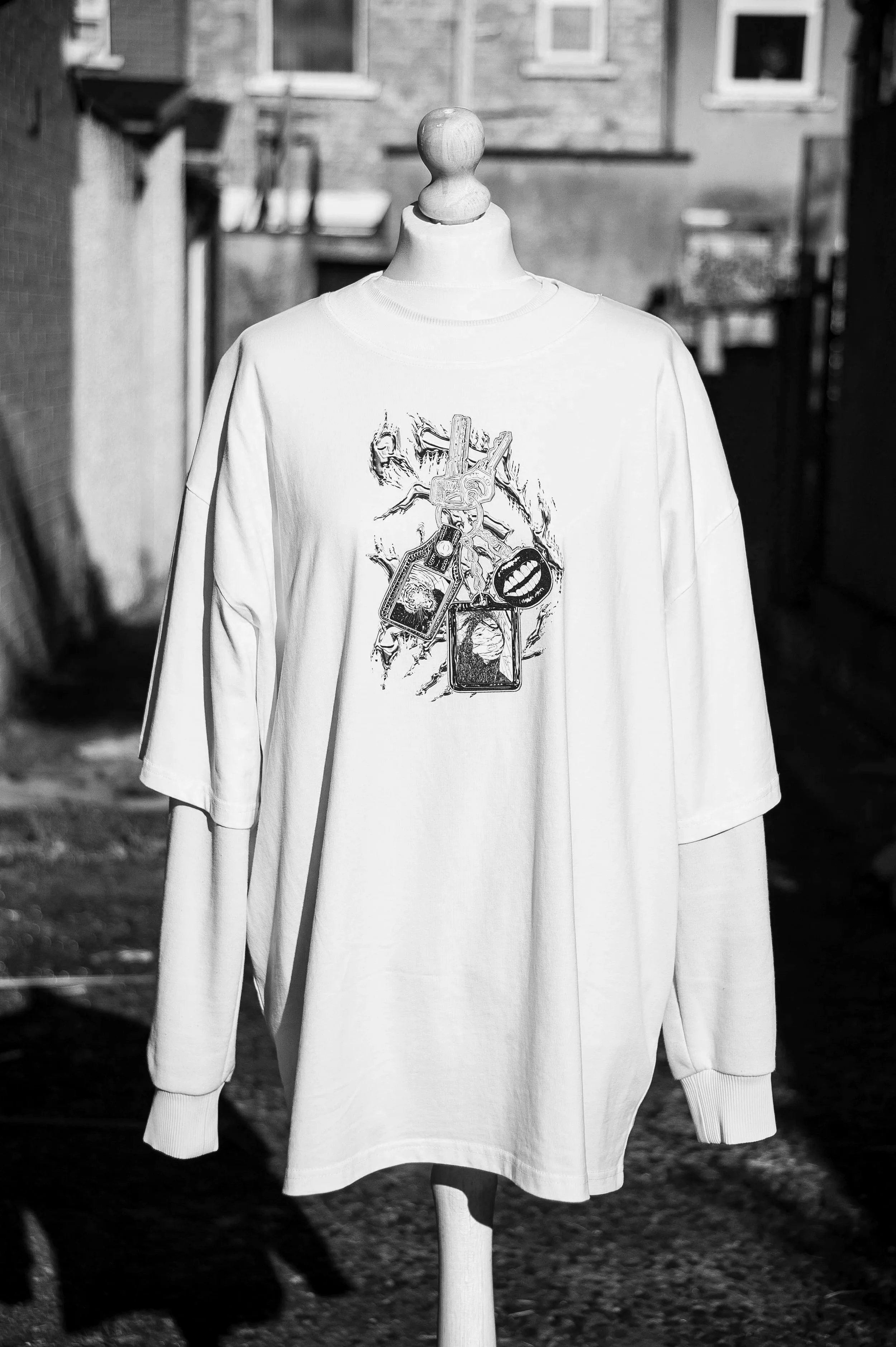 Black-and-white photo of a mannequin wearing a white long-sleeve graphic shirt in a clothing store