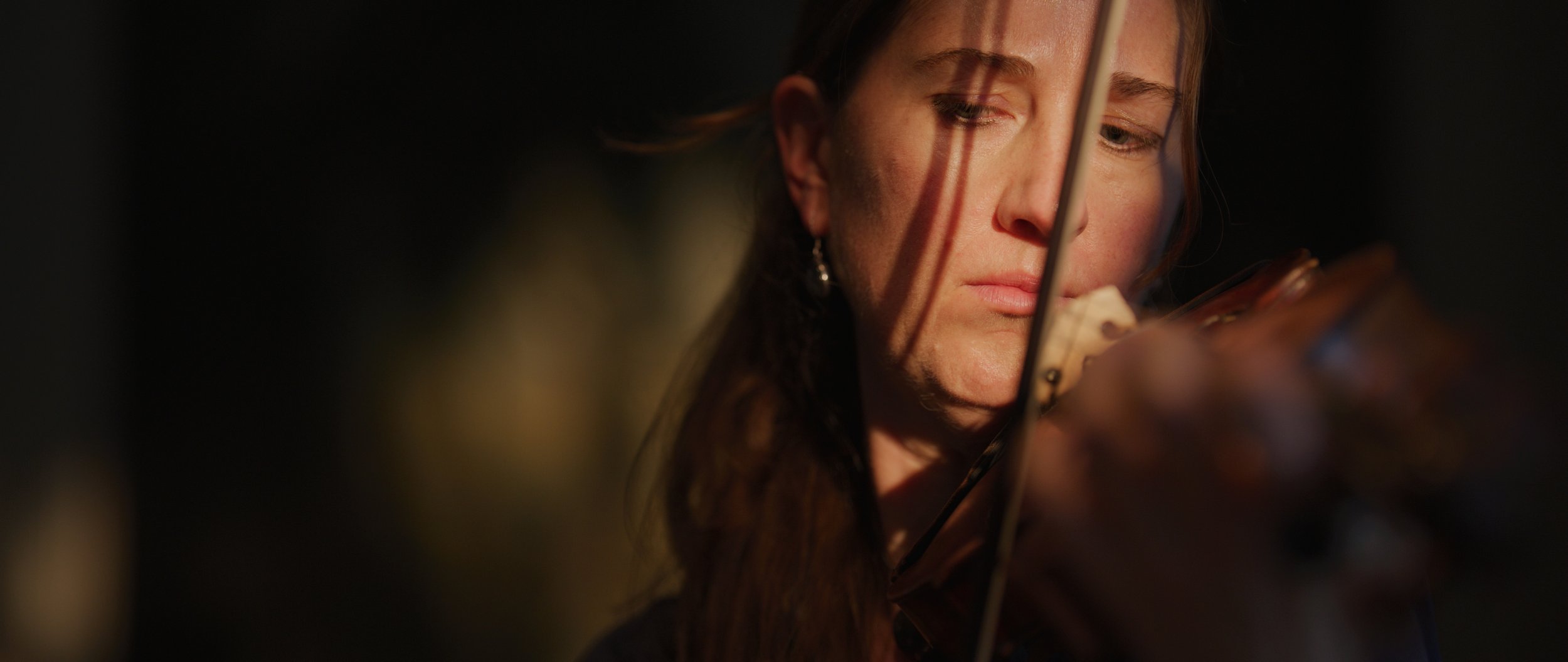 Close-up of person playing violin, focused expression, partial face visible, soft lighting