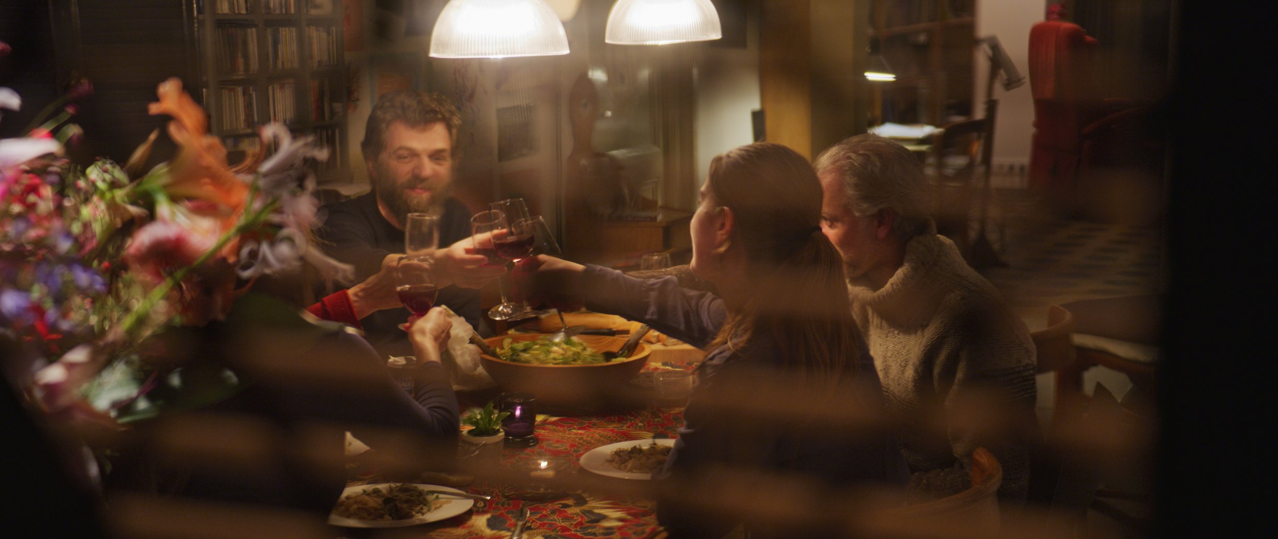 Group of people dining indoors, toasting with wine glasses at a dinner table, ambient lighting.
