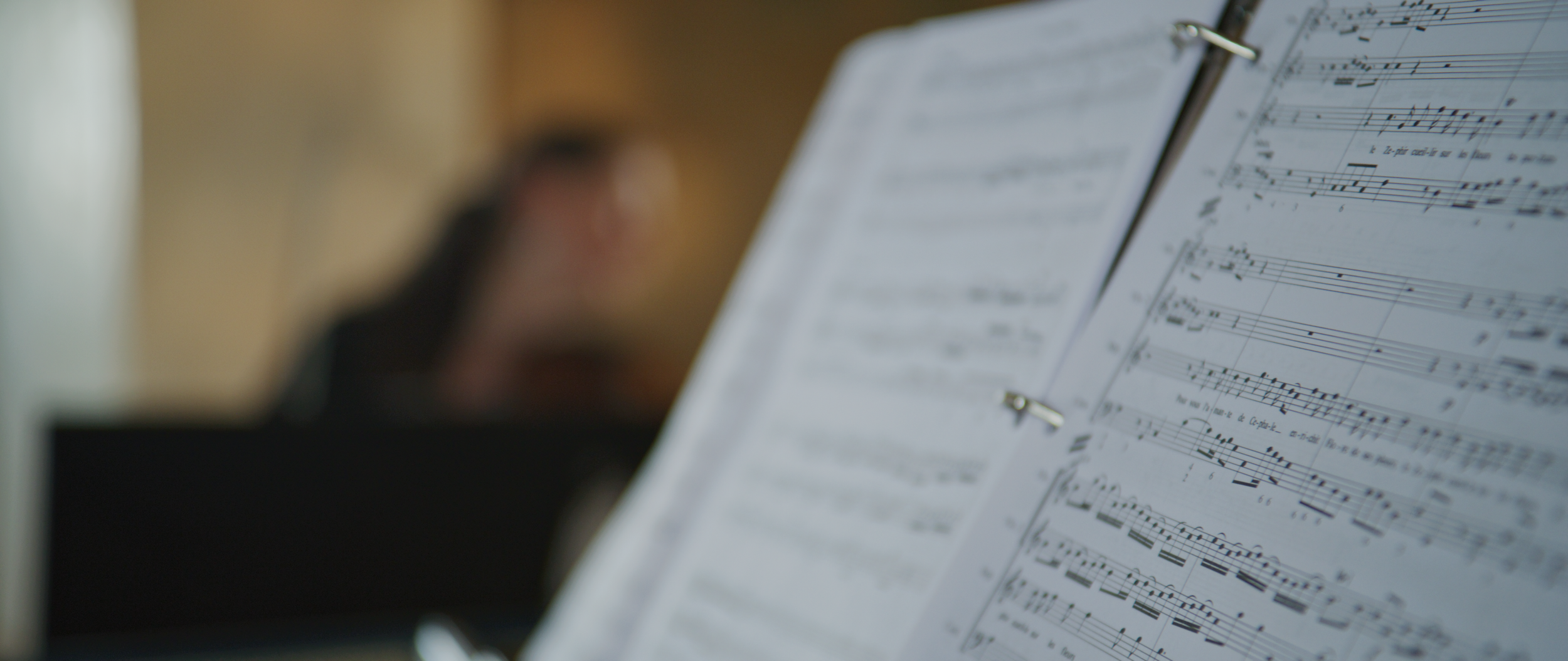 Open binder with sheet music and blurred musician in the background, focus on musical notes.