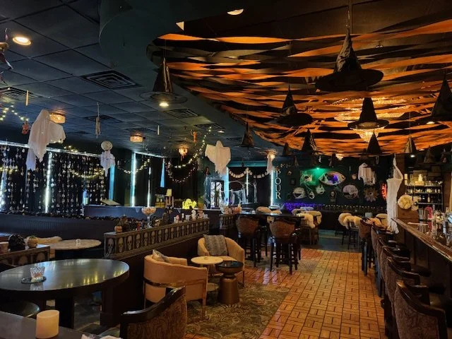Decorated restaurant with Halloween-themed decorations, string lights, and black and orange banners hanging from the ceiling.