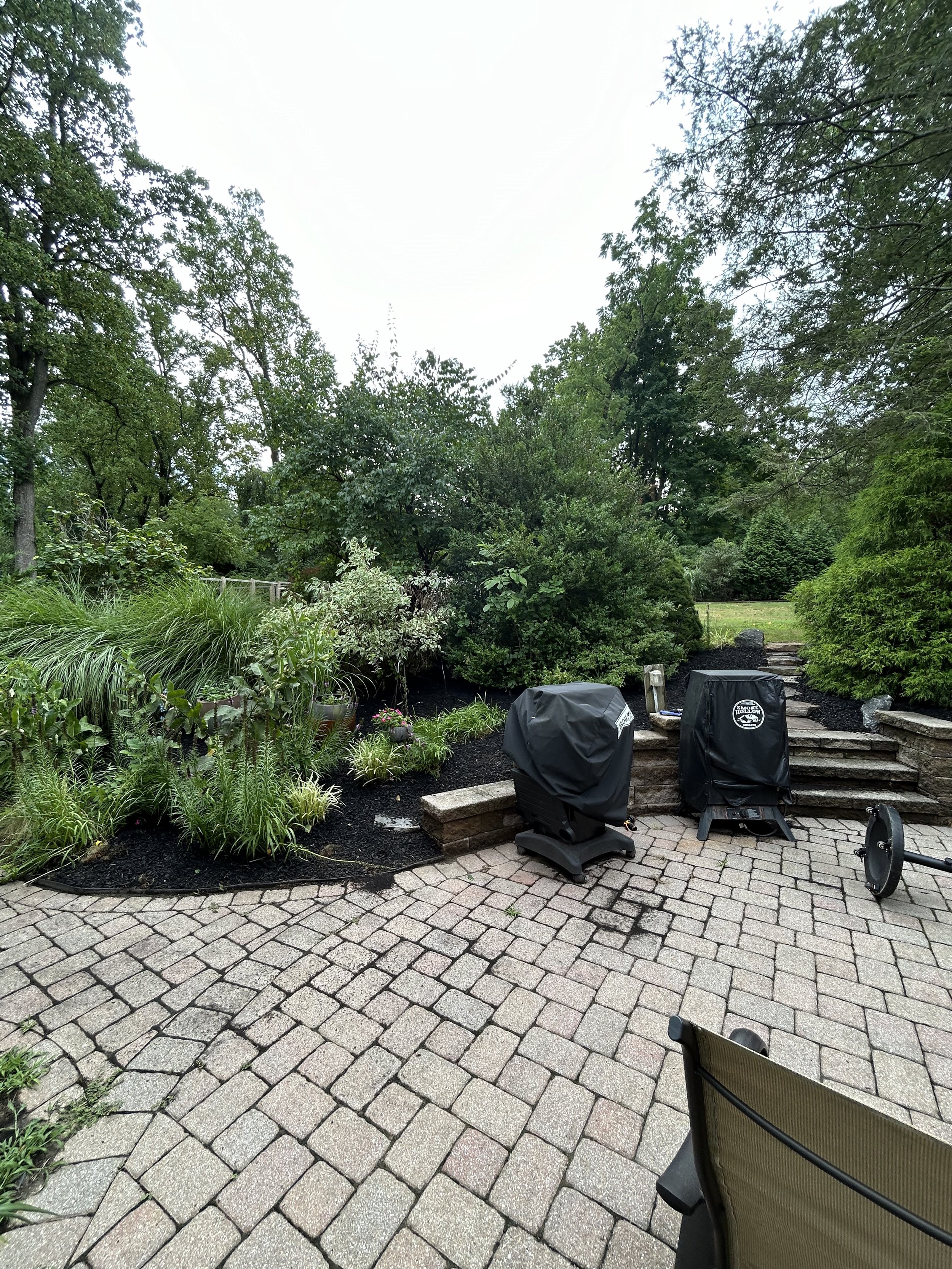 Outdoor patio with stone pavers, covered grills, and surrounding greenery.