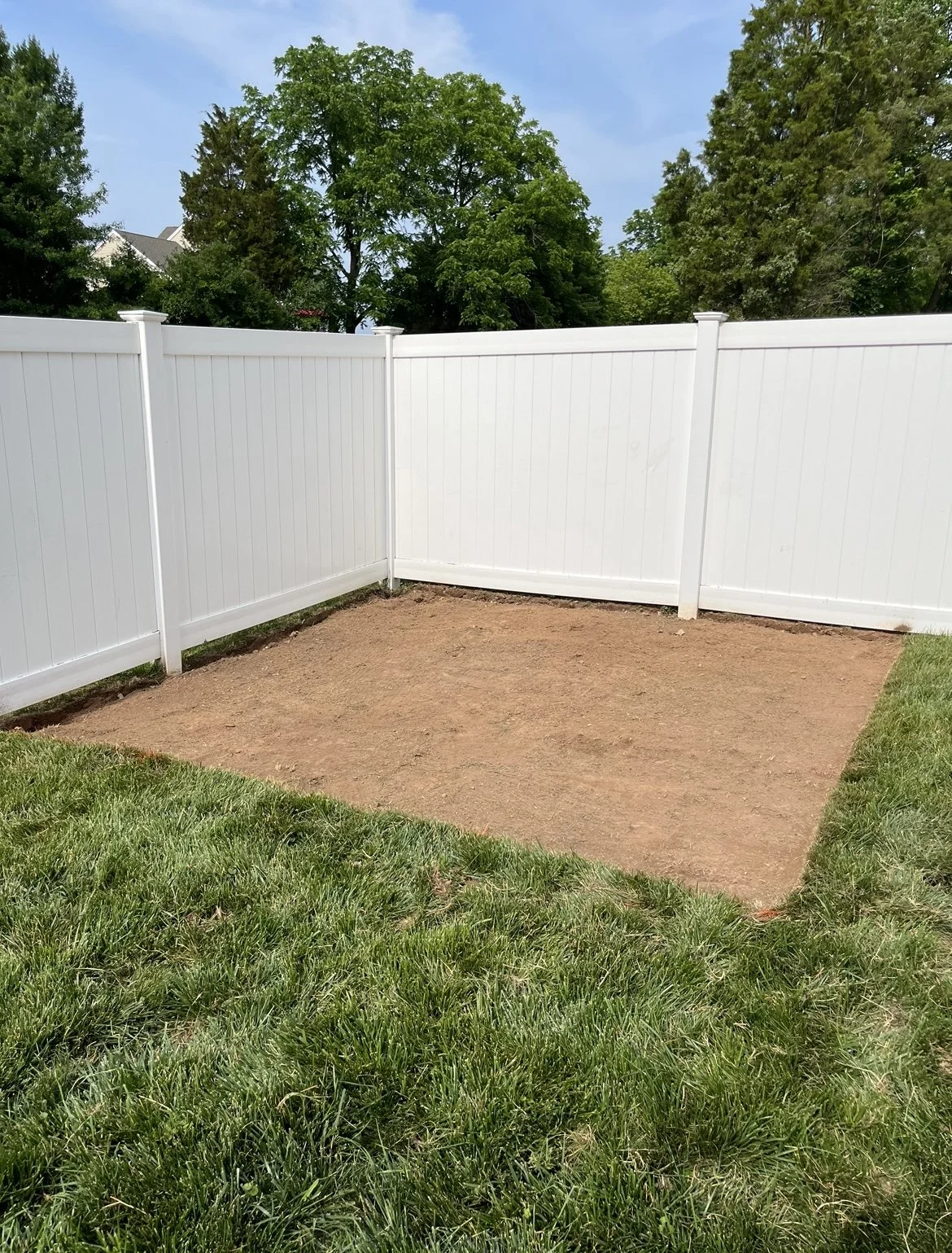 Fenced backyard corner with bare soil and grass