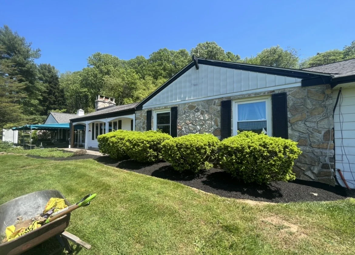 Stone house with black shutters and green bushes under a blue sky
