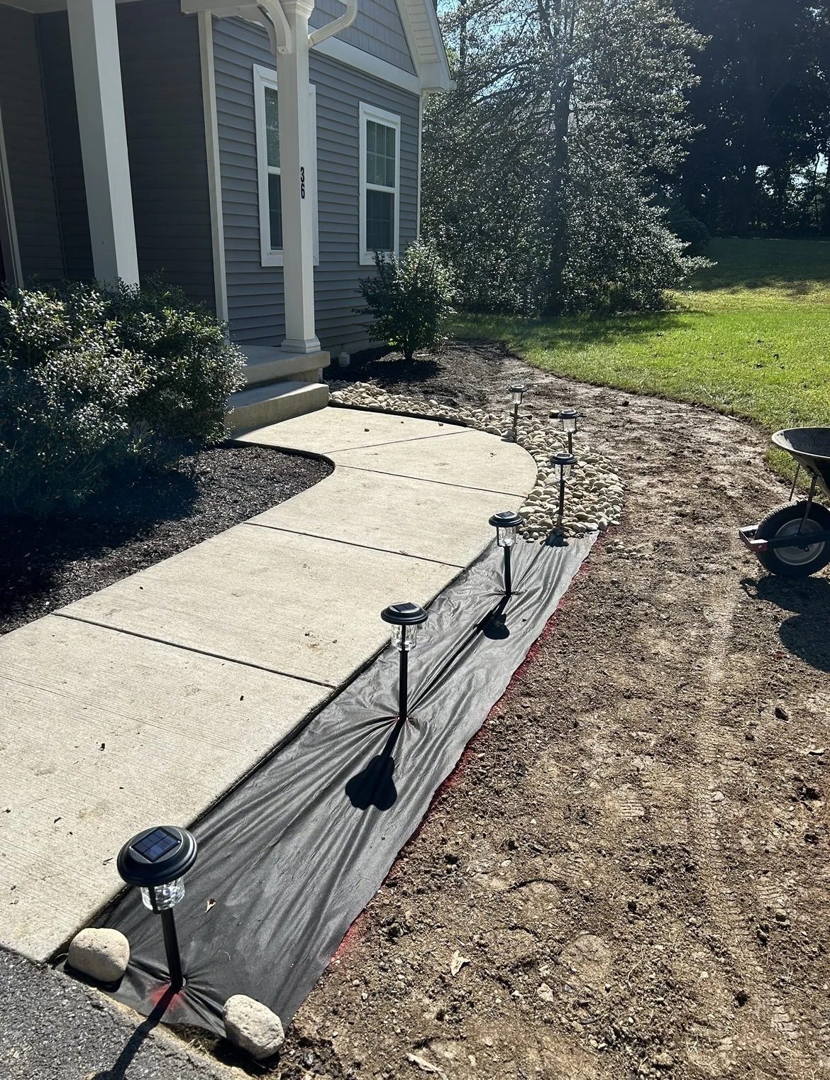 Sidewalk with solar lights and fabric lining beside a house