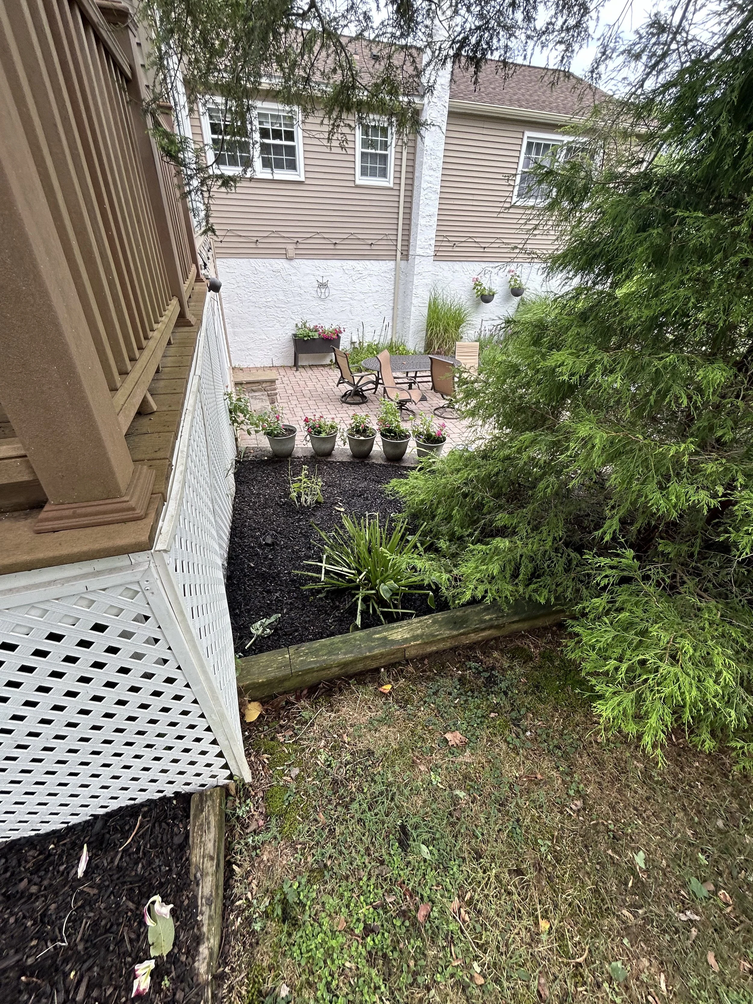 Backyard patio with chairs, planters, and greenery, adjacent to a beige house with white trim and a deck.