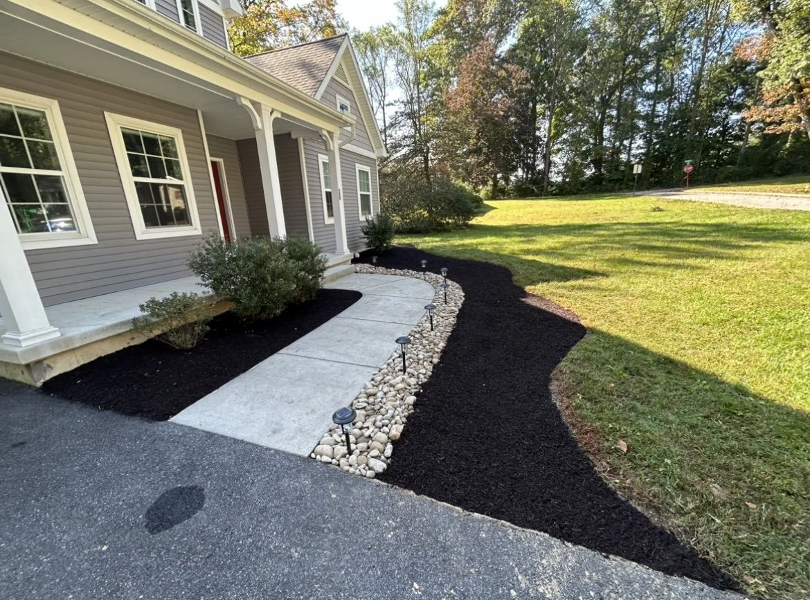 Front yard landscaping with walkway, shrubs, rocks, mulch, and lawn.