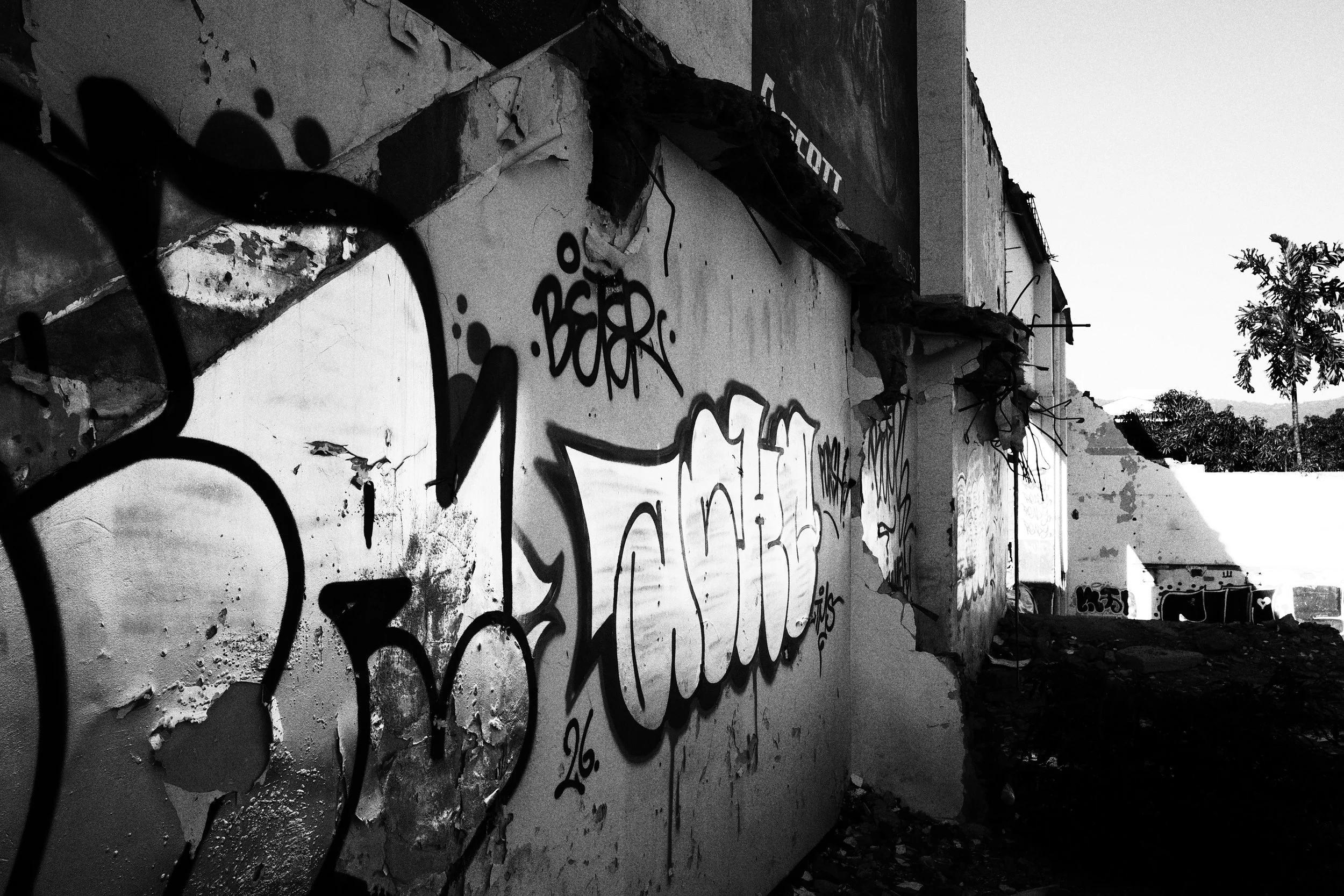 Black and white photo taken along the cracked exterior wall of a demolished building in Medellín, where layered graffiti stretches into the distance above piles of rubble.