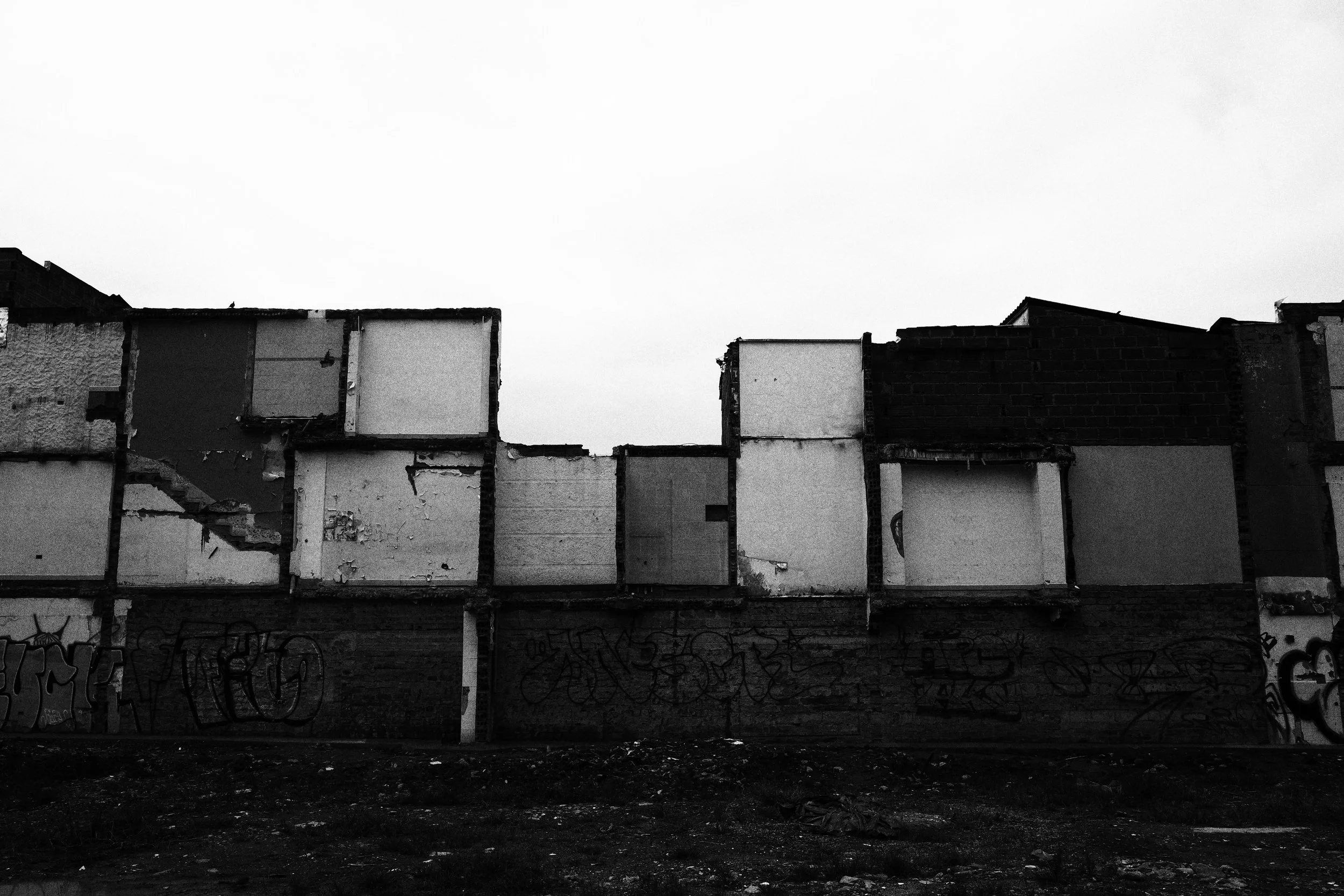 Black and white panoramic photo of partially demolished row houses in Medellín, their exposed rooms forming a grid of empty rectangles above graffiti-covered walls.