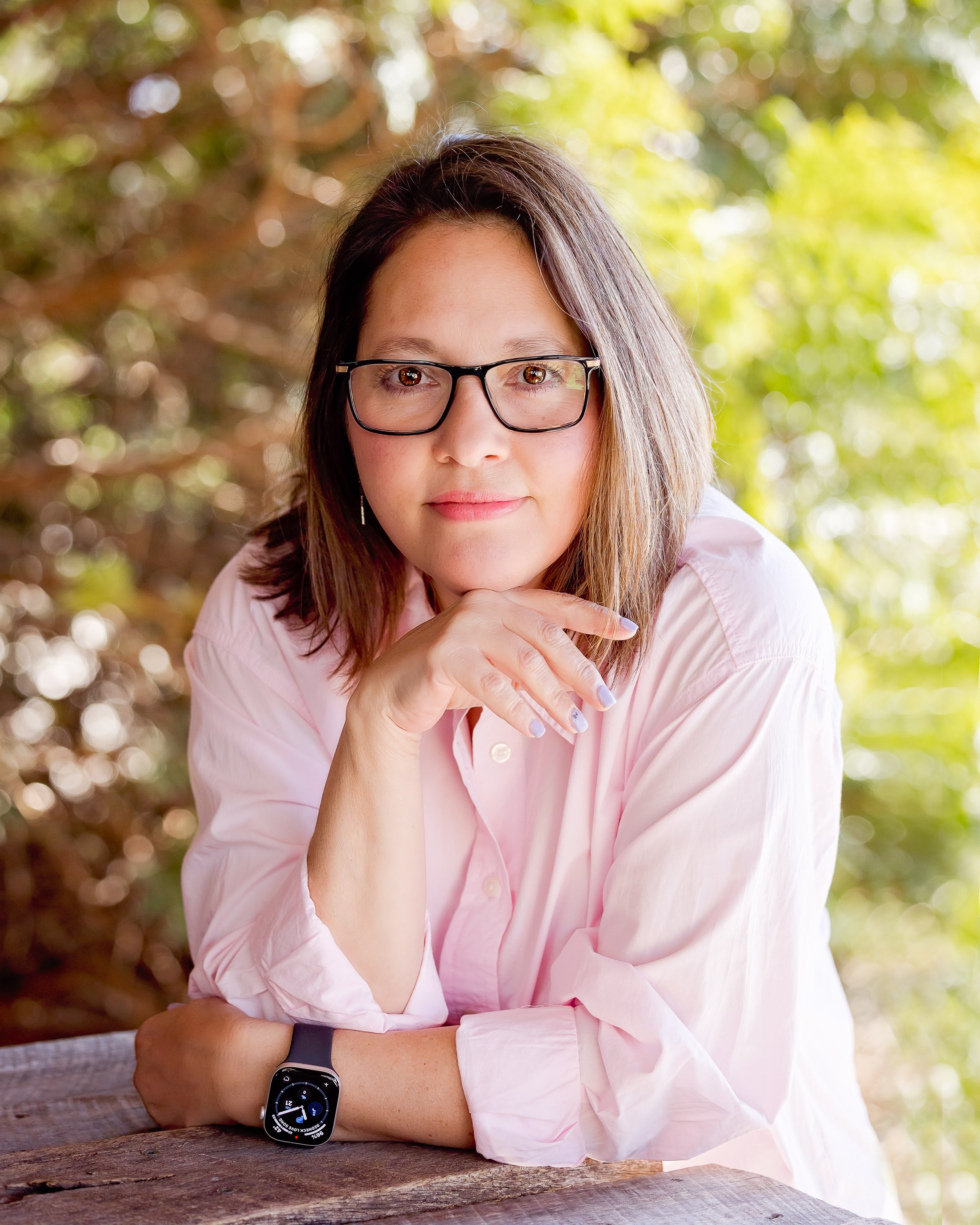 woman in a pink shirt and glasses with her hand under her chin smiling at the camera for a casual headshot