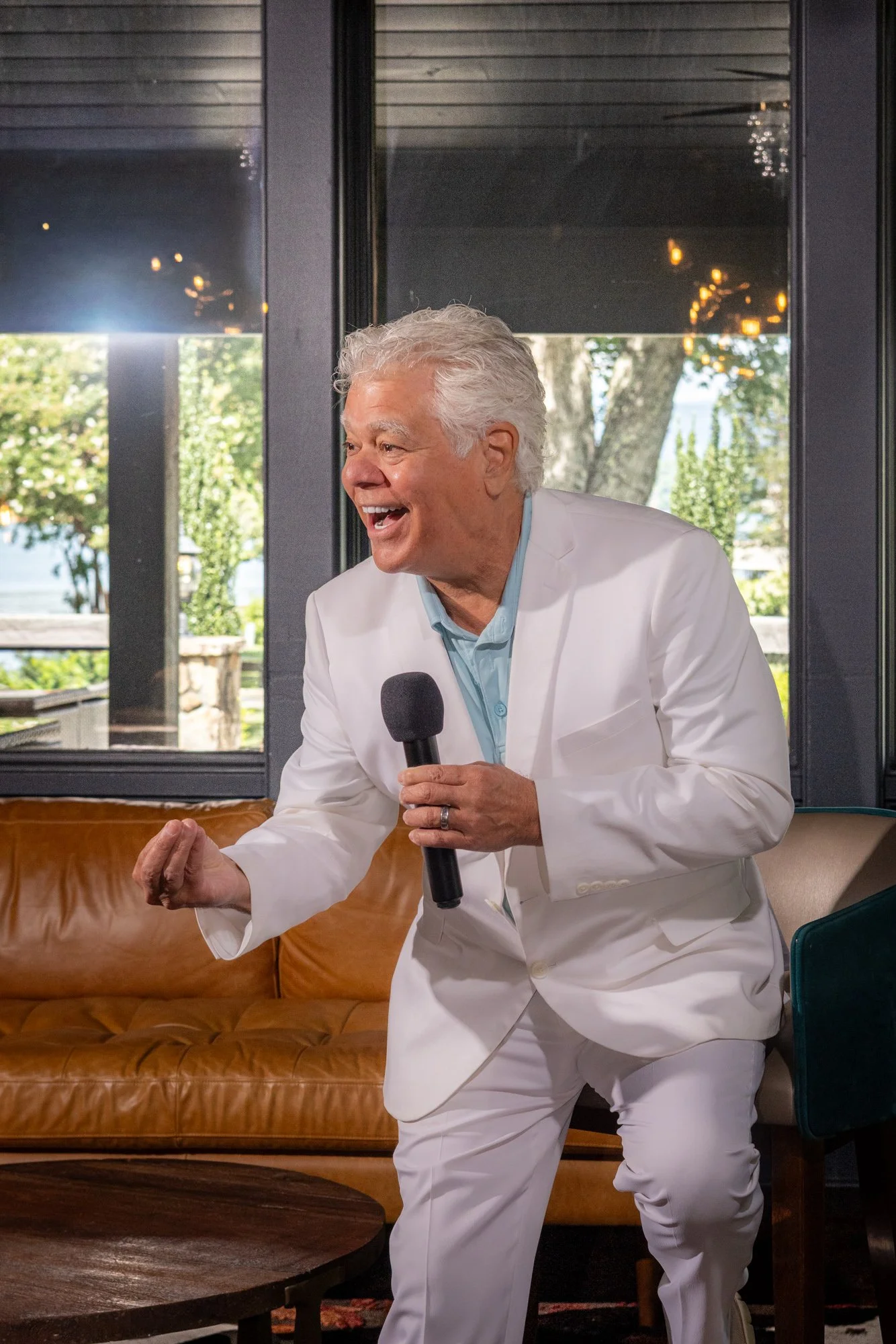 Singer in a white suite suit holding a microphone singing with a smile on his face