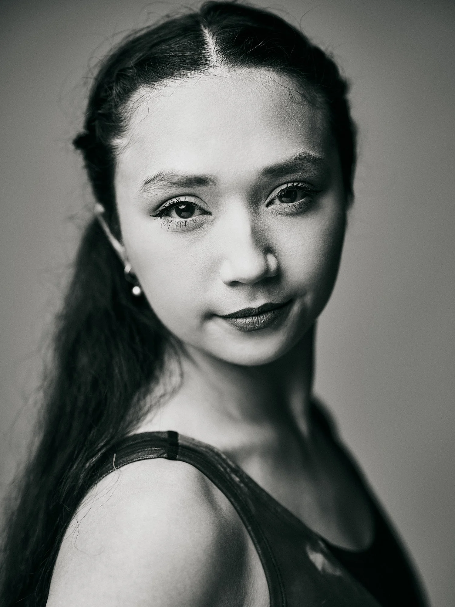 Black and white portrait of a young woman with long hair and earrings, looking directly at the camera.
