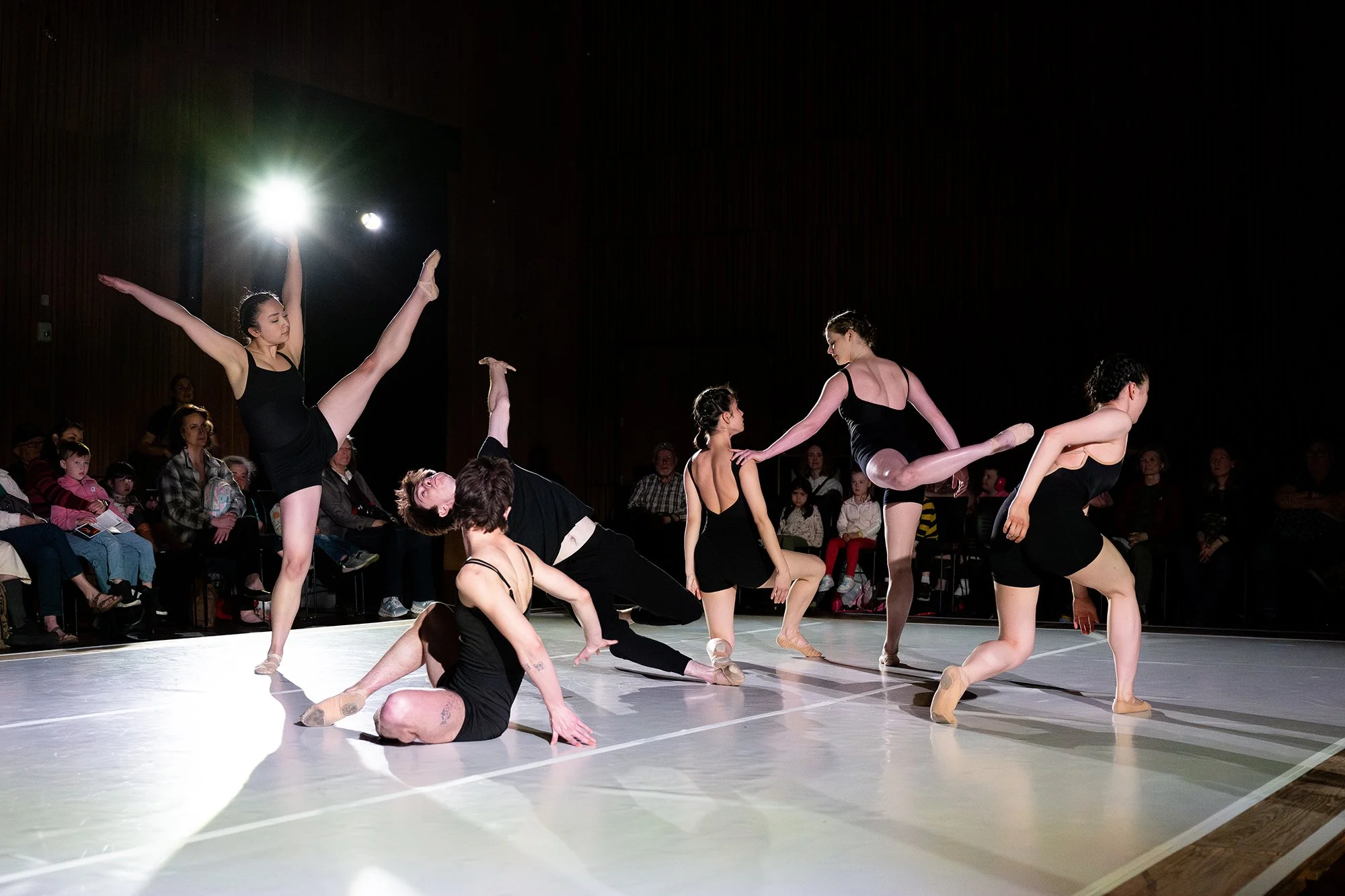 Ballet dancers performing on stage with audience watching in background.