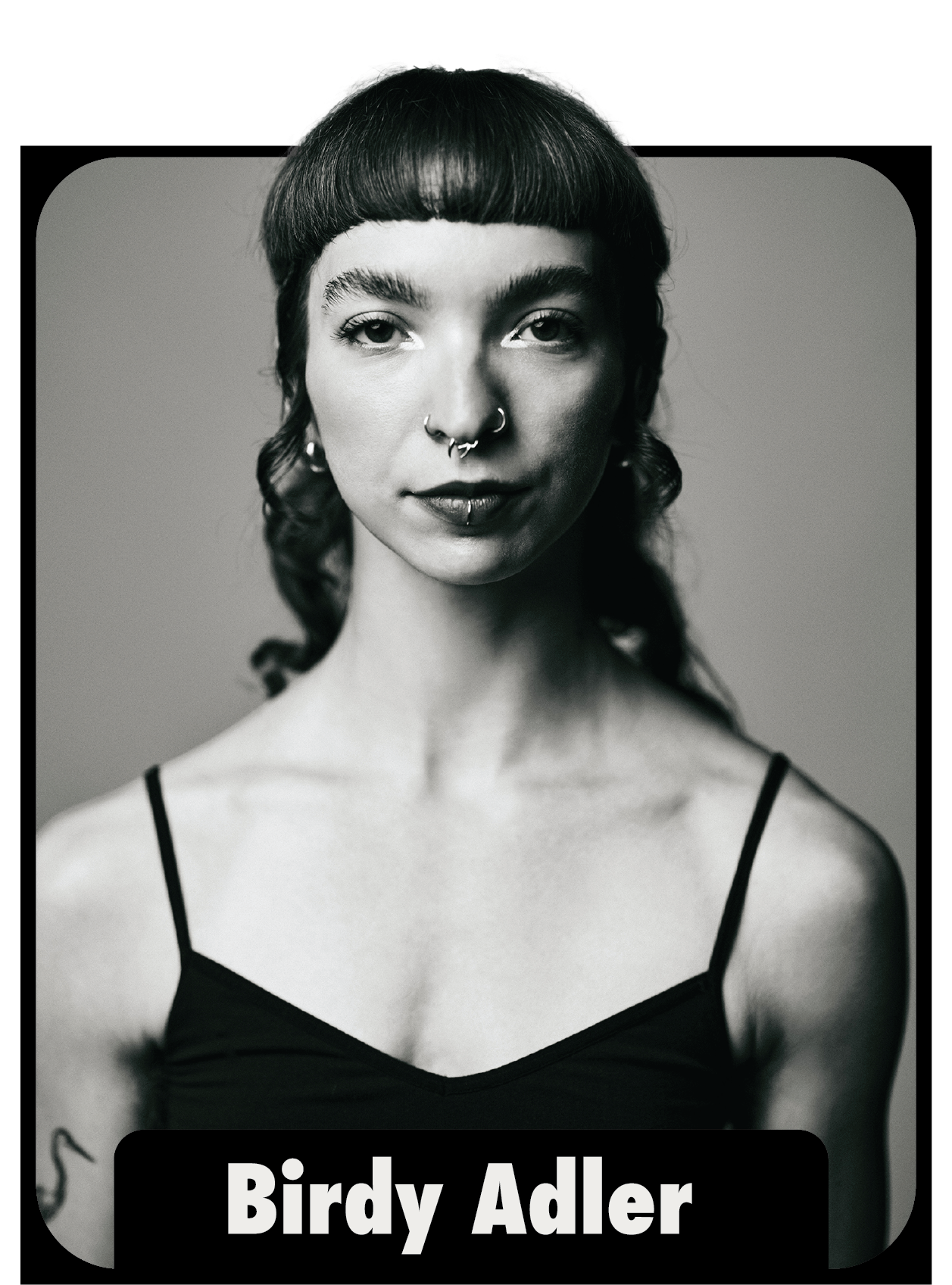 Black and white portrait of a woman with short dark hair and several facial piercings, wearing a black spaghetti strap top, with her hair styled in loose curls, and a tattoo visible on her left upper arm, with the name Birdy Adler at the bottom.