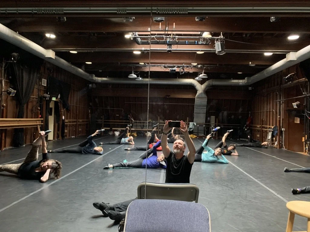 Group fitness class with participants stretching on the floor in a dance studio, taking a selfie in the mirror