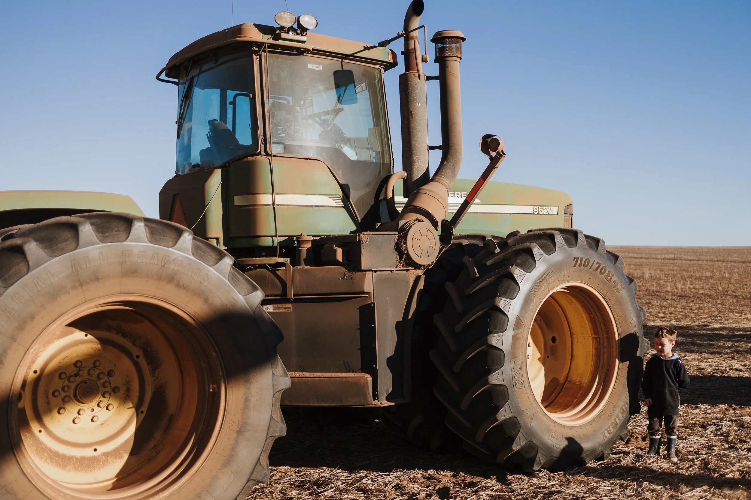 Large tractor parked in a paddock with a child standing beside the front tyre