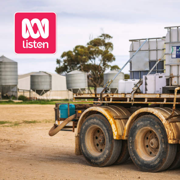 Farm truck with tanks and equipment on dirt field, grain silos in background,