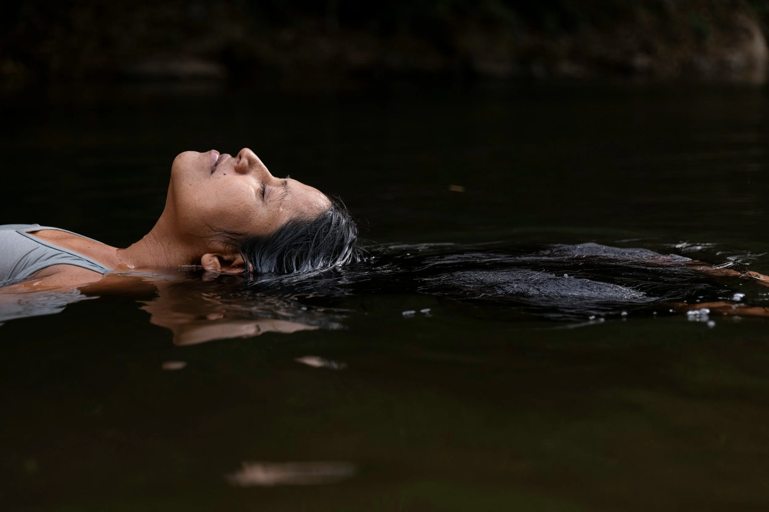 A woman floats in a dark pool of water