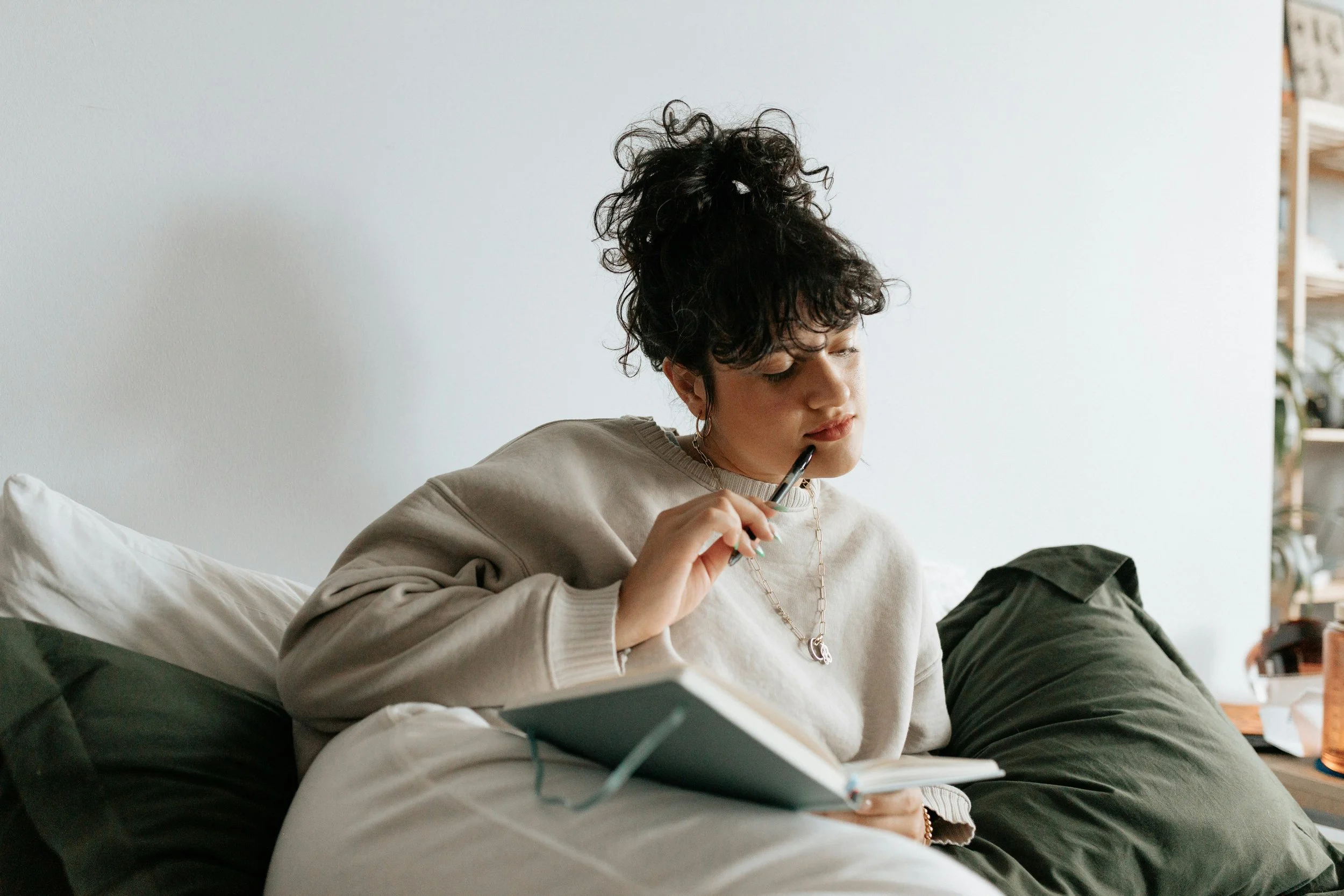 A woman pensively sits up an open notebook and a pen on a green bed