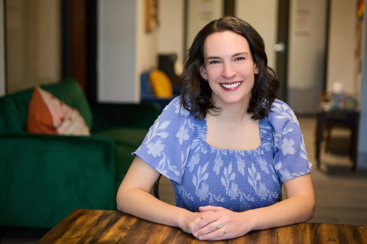 Dr. Bridget poses for a professional headshot, her arms resting on a table, and a welcoming, kind smile on her face