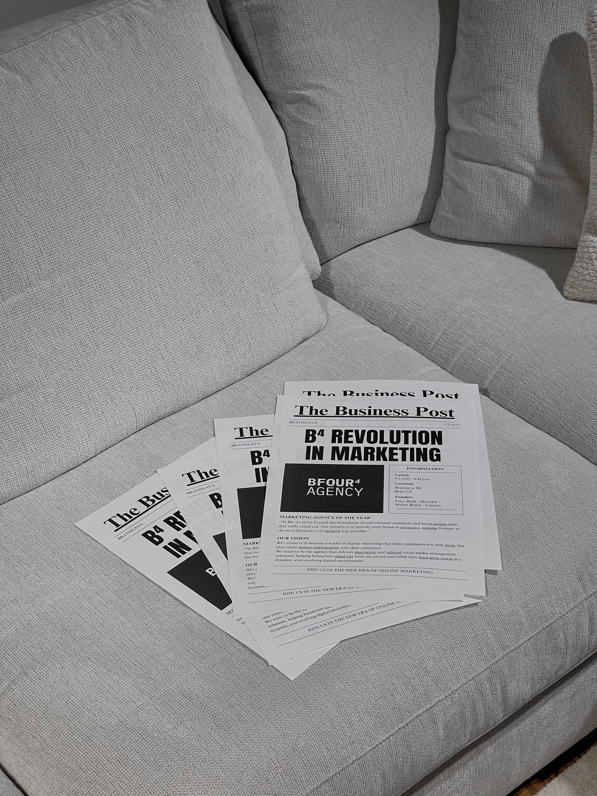 Several copies of a newspaper titled 'The Business Post' are arranged on a light gray fabric sofa.