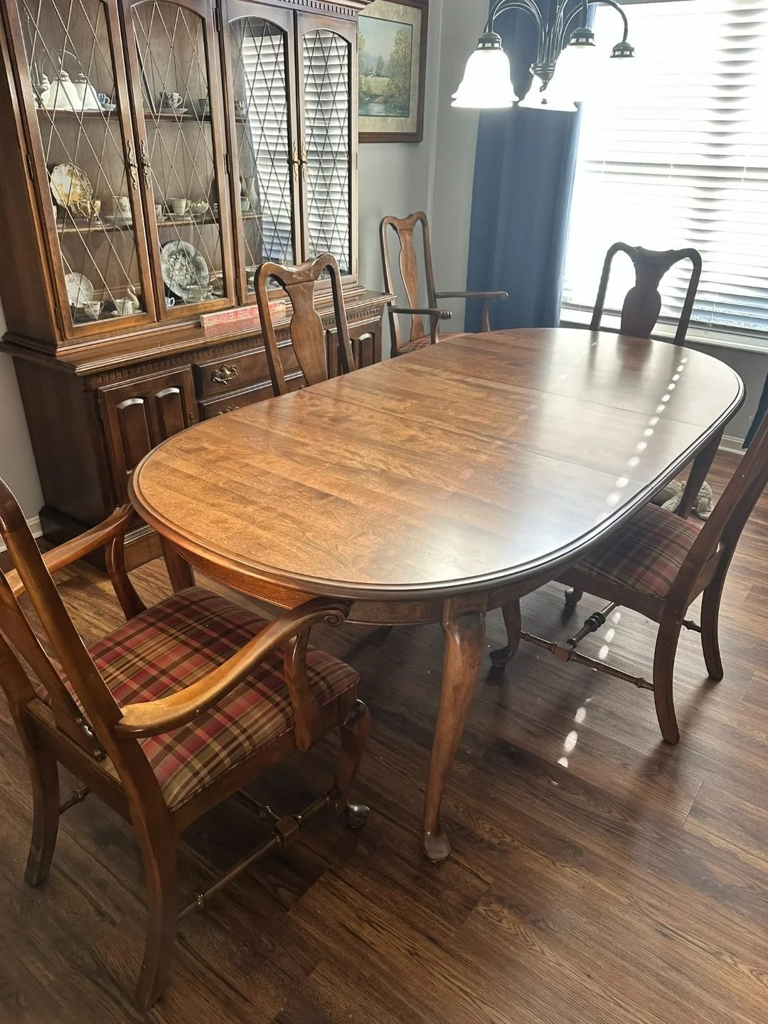 Traditional wood dining table with matching chairs in a dining room, with a china cabinet and window light
