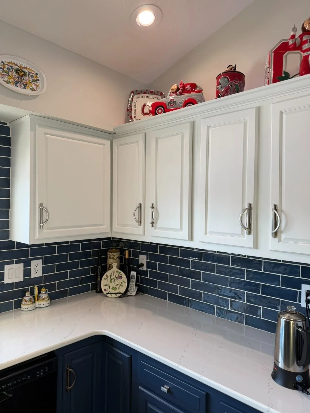 Kitchen range wall with white upper cabinets, blue lower cabinets, navy subway tile backsplash, and stainless appliances