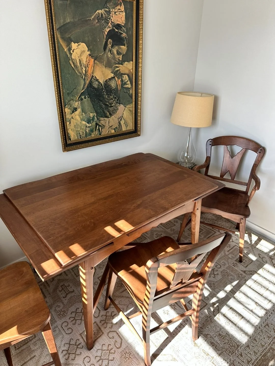 Detail shot of a solid wood dining chair with curved arms and a carved back, shown in warm natural light next to a matching table