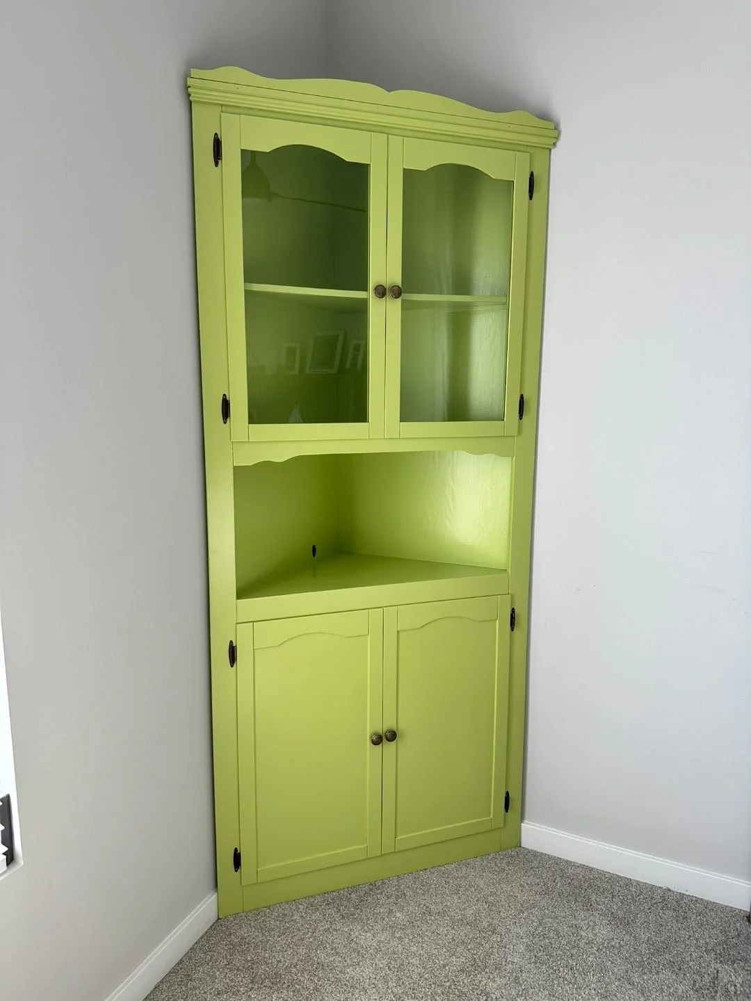 Lime green painted corner hutch/cabinet with glass upper doors and closed lower storage, a bold statement piece that brightens up a neutral room and adds functional display space