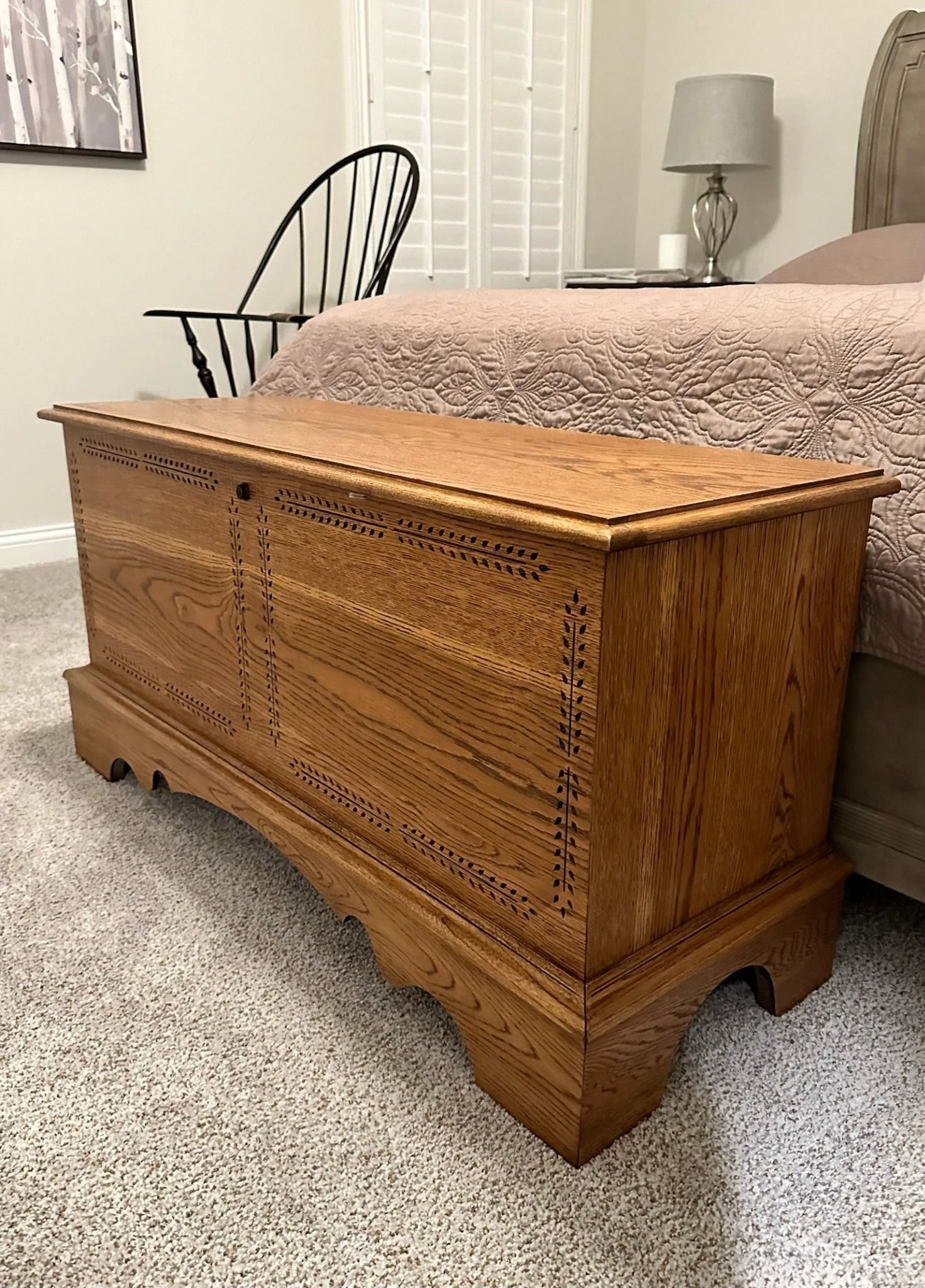 A refinished wooden hope chest with intricate detailing from Craft & Revive in Dayton, OH, placed at the foot of a cozy, well-styled bed