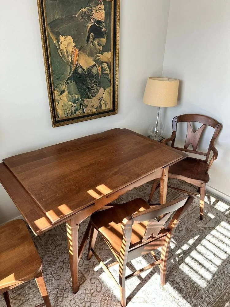 Detail shot of a solid wood dining chair with curved arms and a carved back, shown in warm natural light next to a matching table
