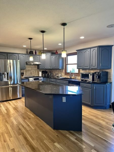 A full kitchen cabinet refinishing that transforms the space with a rich blue/gray tone and a cohesive, updated look. The refreshed cabinetry pairs well with stainless appliances and a dark countertop, giving the room a more current, high-end feel wi