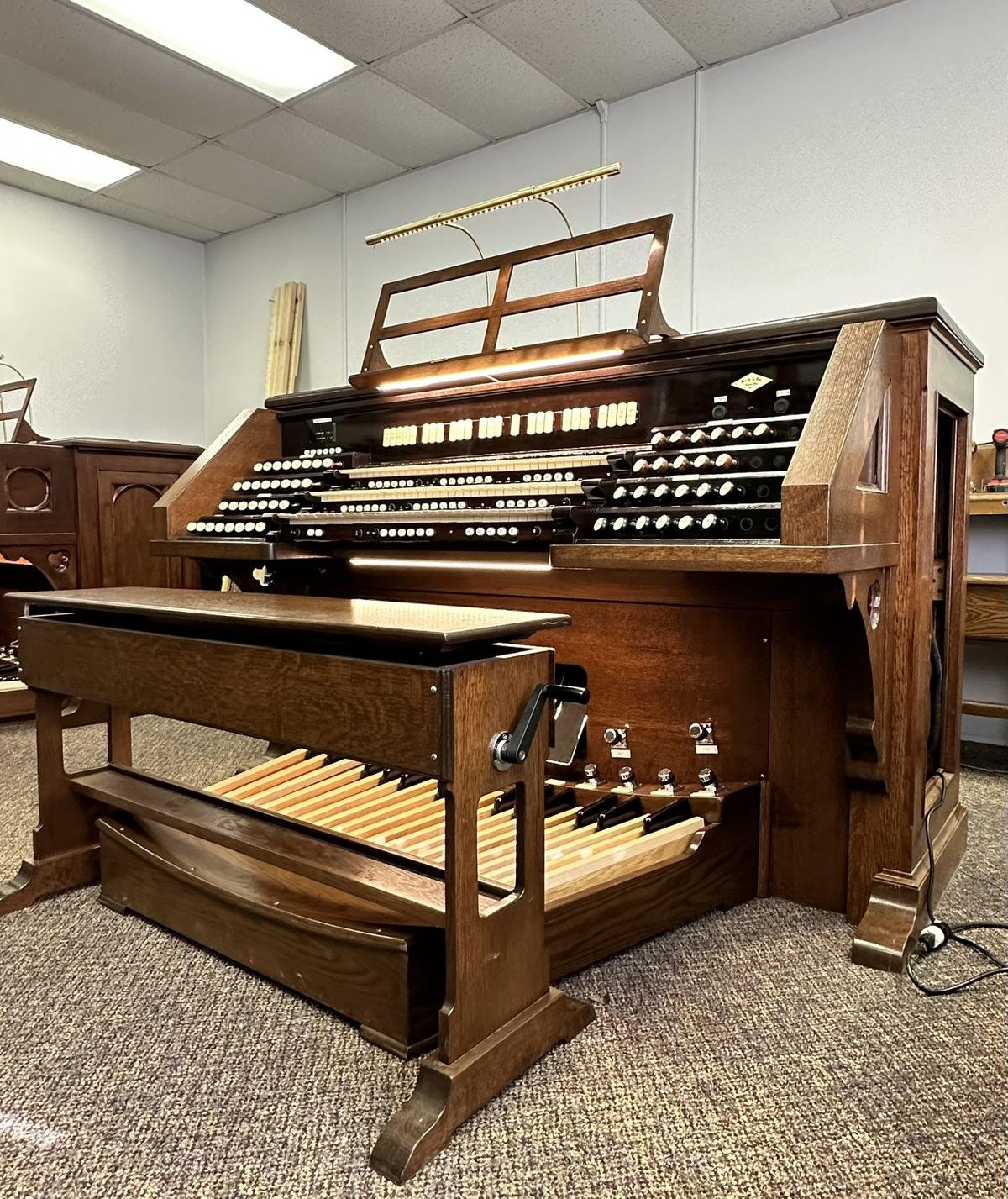 A beautifully refinished wooden organ console with intricate controls from Craft & Revive in Oakwood, OH, set in a well-lit workshop