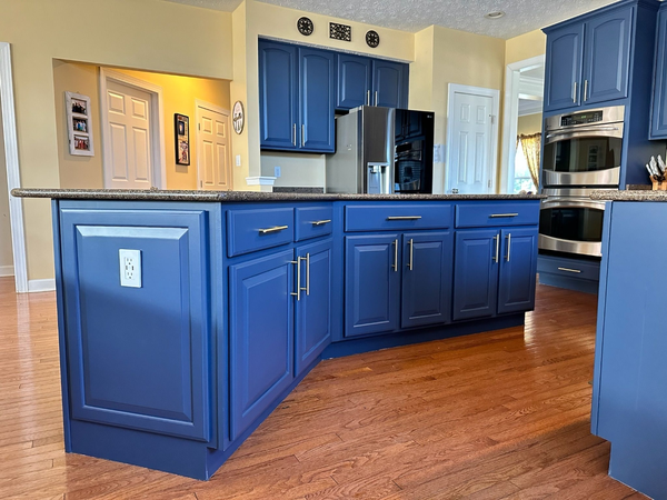 Kitchen with blue cabinets, stainless steel refrigerator, double oven, granite countertops, hardwood floor, and yellow walls.