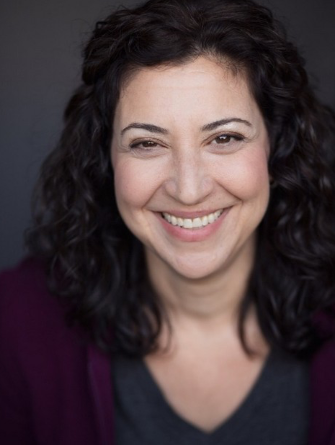 Close-up portrait of a woman with curly dark hair smiling against a dark background.