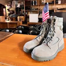 A pair of gray combat boots with an American flag attached to them, placed on a wooden surface in a bar or restaurant setting.