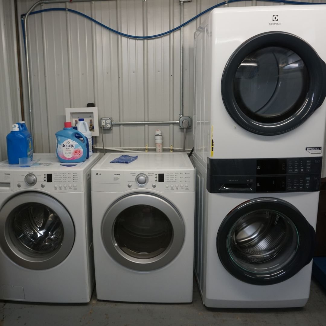 Laundry room with three modern washing machines and dryers, laundry detergent bottles on top, metal wall and floor.
