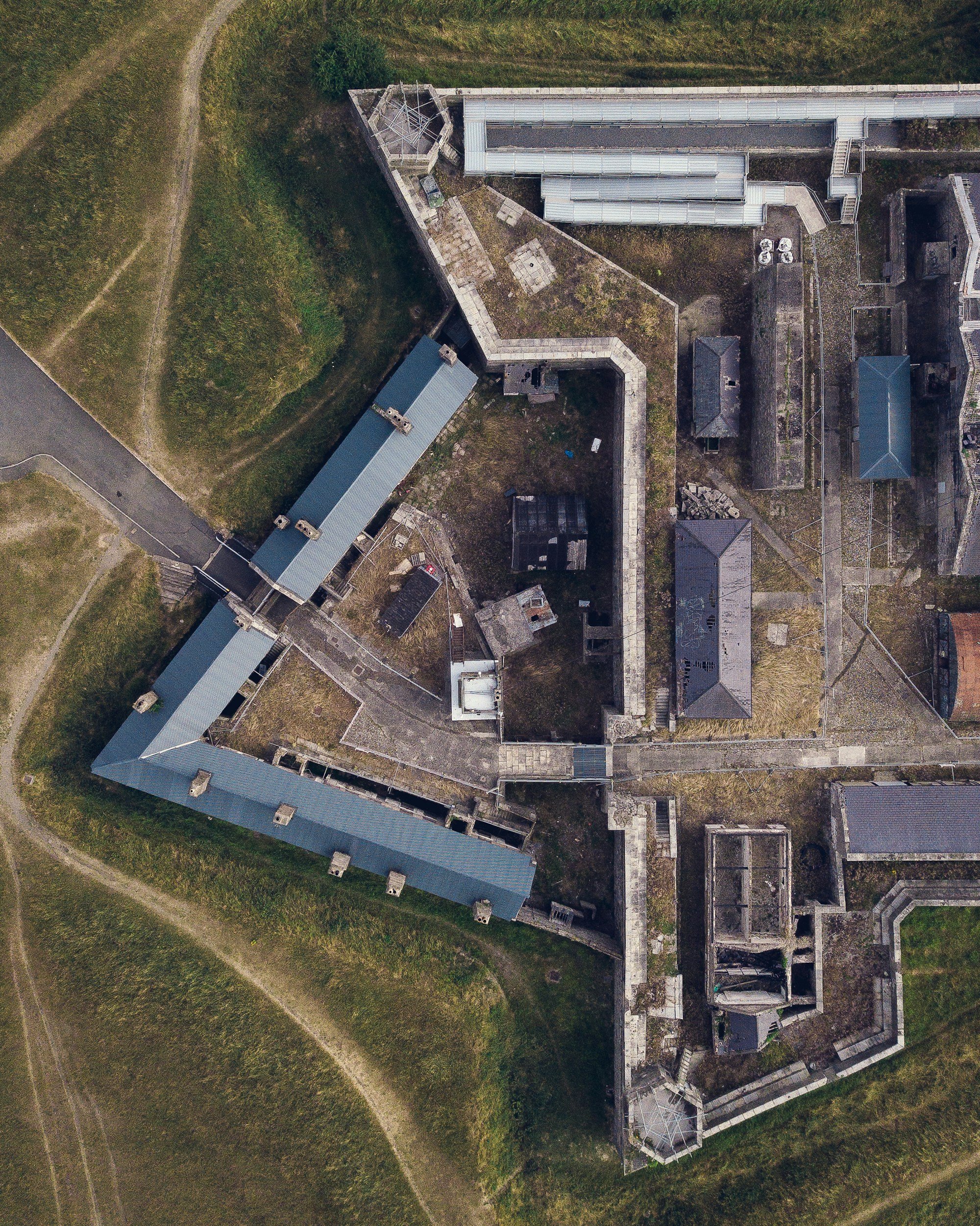 Aerial view of a historic castle with stone walls, several buildings with metal roofs, and lush green surroundings.